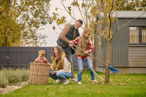 Man-With-Daughter-Raking-Leaves-Woman-With-Child Happy family spending time outdoors.