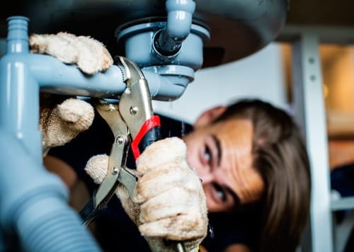 Proven Ways To Keep Fire Ants Out Of Your Home 4 Person in gloves uses wrench to fix light blue plumbing pipes under a sink.