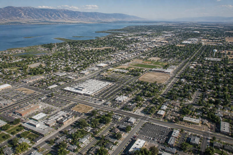 Aerial view of a sprawling green town bordering a vast lake with distant mountains.